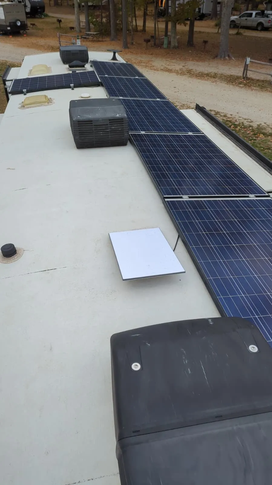 White Starlink Gen 3 residential dish sitting on an RV roof between the air-conditioner covers and a row of solar panels
