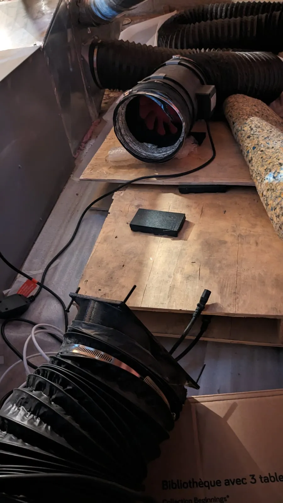 Flex duct and an inline fan being routed across plywood in the crawl space, with the duct ends not yet connected