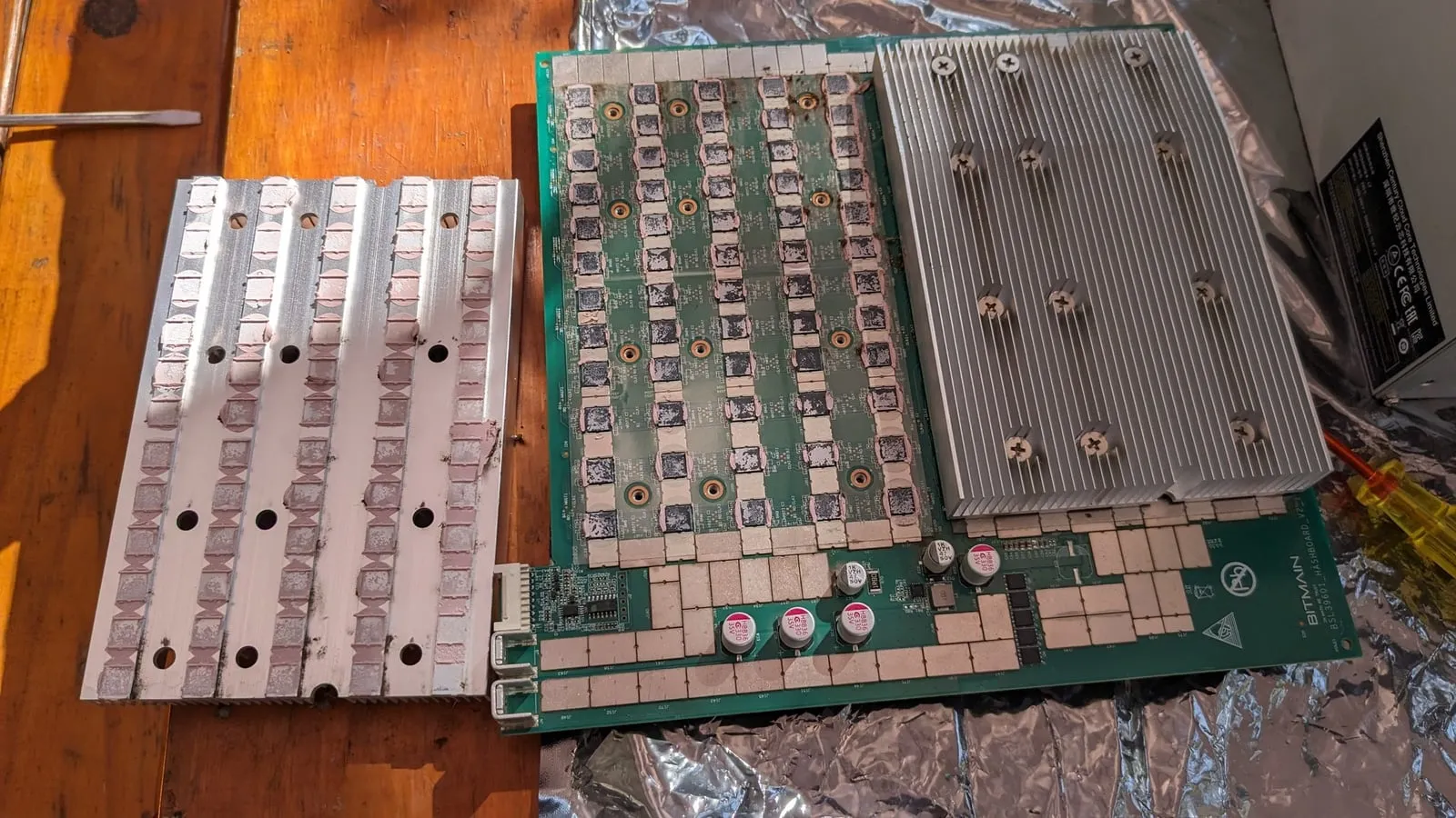 A hash board laid out next to its two heatsinks, which have been lifted off